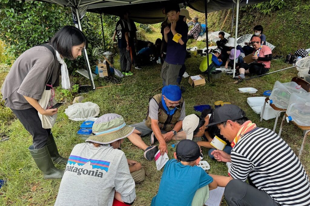 つかまえた水生生物の種や名前を、図鑑と照らし合わせながら確認していく。写真中央は、アドバイザーとして参加した高知昆虫研究会の別府隆守さん。