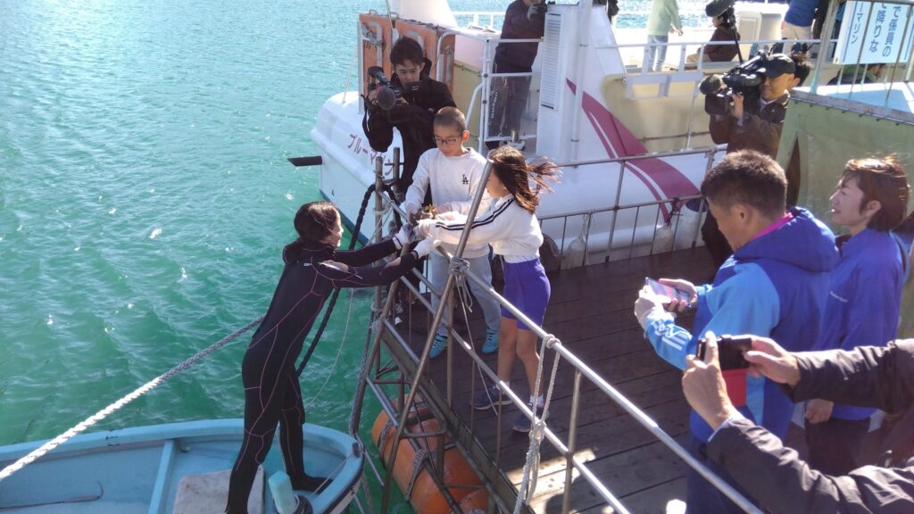 ミドリイシサンゴの苗が植えられた台石をダイバーに手渡す子どもたち。サンゴを載せた台石は、漁船で沖に運ばれ、ダイバーの手で海底に沈められる。
