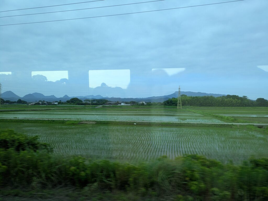 中津から別府へ向かうJR日豊本線の車窓から。中津から宇佐にかけて、左右に広大な水田の景色が広がる。右手奥の丘陵は八面山。