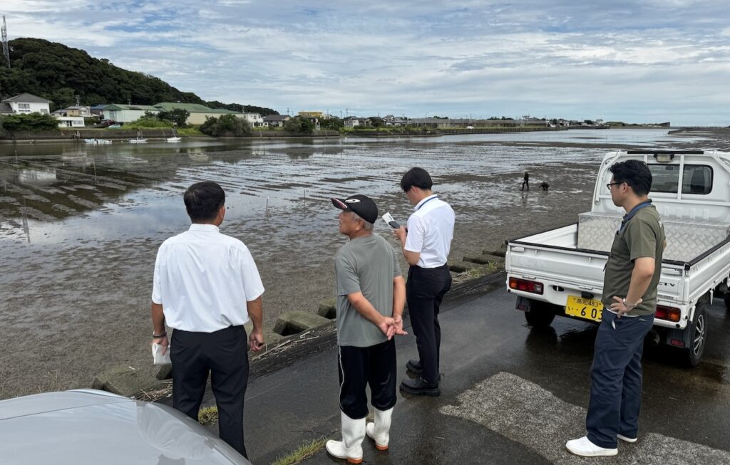 竹島川干潟で、アオサノリ養殖の説明をする四万十川下流漁業協同組合の沖組合長（左から二人め）。